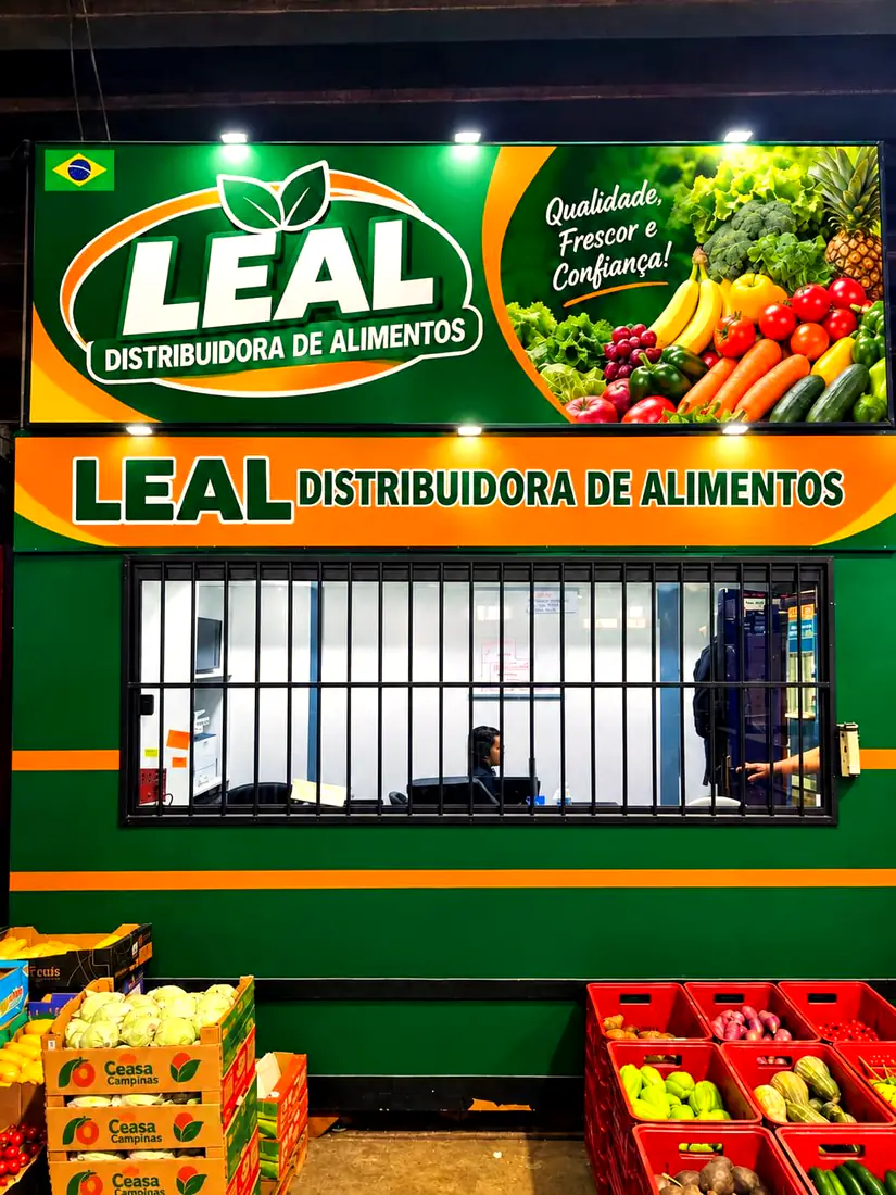 Fachada da Leal Distribuidora de Alimentos, em verde e laranja, com caixas de hortifrúti na frente